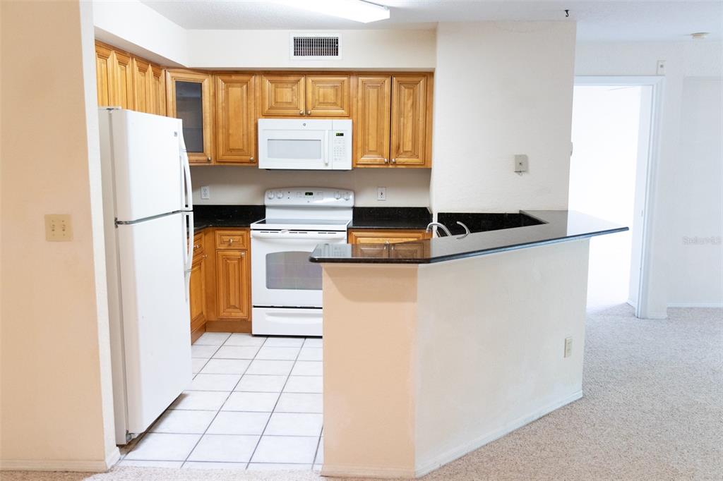 A kitchen with wood cabinets, white appliances, black countertops, and a breakfast bar — 822 CAMARGO WAY UNIT 208, ALTAMONTE SPRINGS, FL