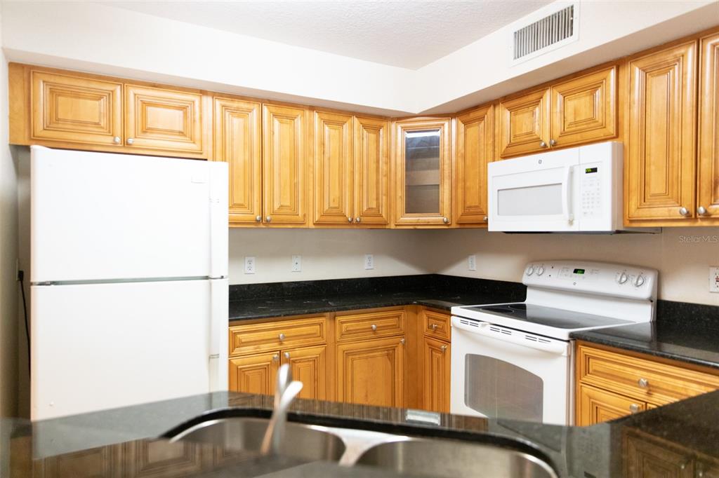 A kitchen features honey-oak cabinets, black granite countertops, and white appliances — 822 CAMARGO WAY UNIT 208, ALTAMONTE SPRINGS, FL