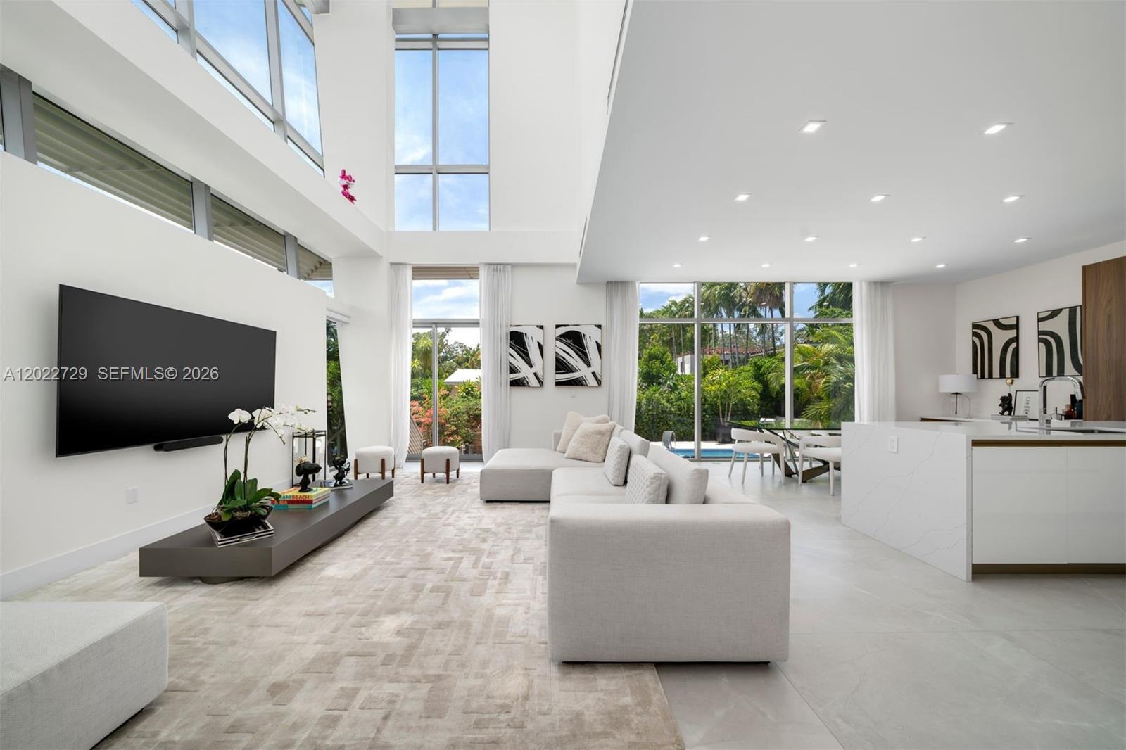A modern, high-ceilinged living room features a large television, white sectional sofa, and floor-to-ceiling windows — 1201 W 47th St, Miami Beach FL 33140, MIAMI BEACH, FL