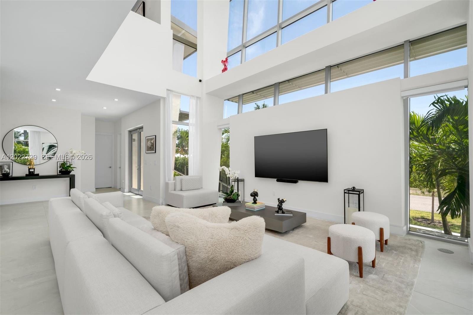 A modern living room features high ceilings, floor-to-ceiling windows, and white minimalist furniture — 1201 W 47th St, Miami Beach FL 33140, MIAMI BEACH, FL