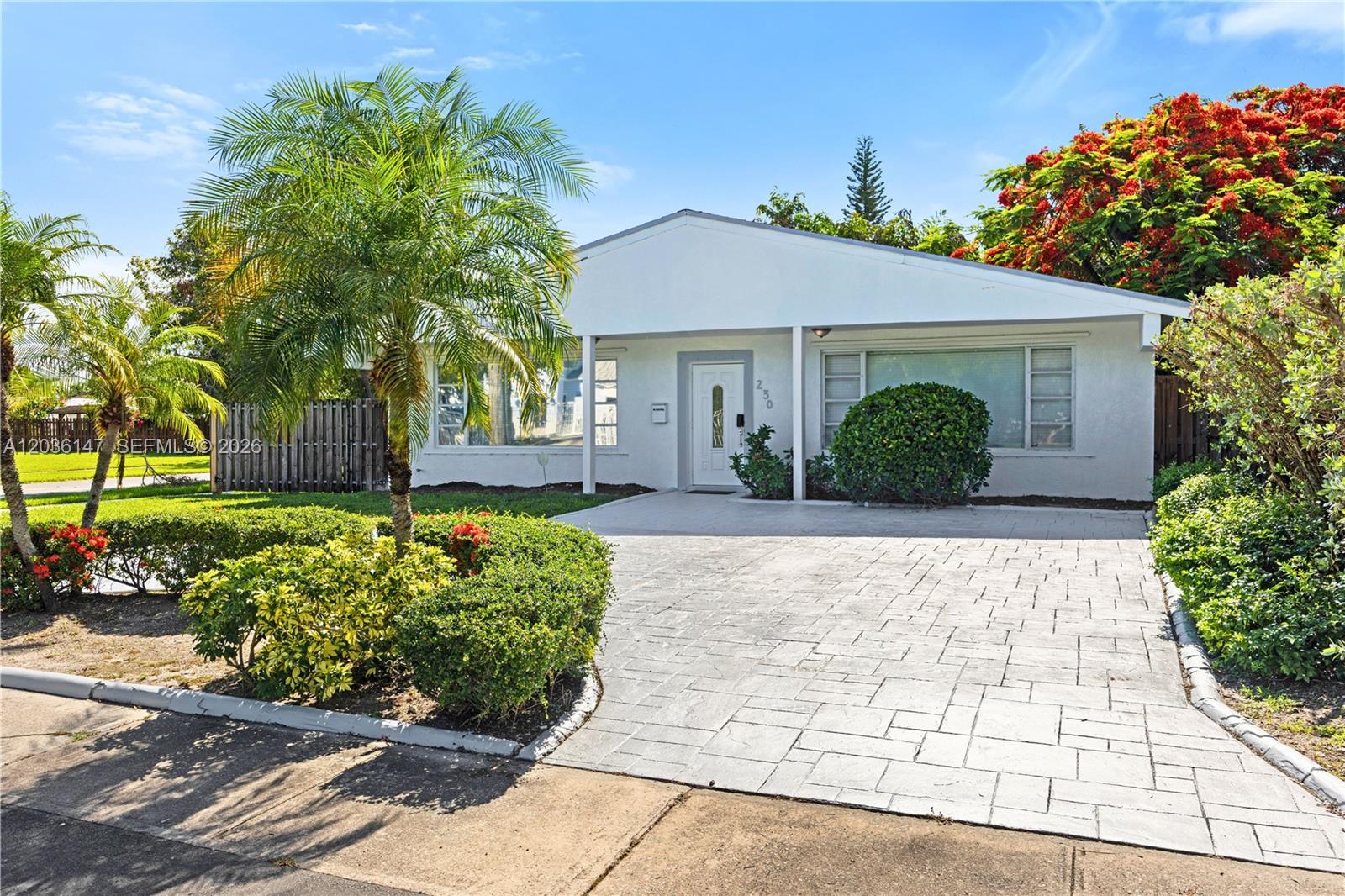 A single-story white house features a paved driveway, a palm tree, and a landscaped yard — 230 NE 5th Ave, Dania Beach FL 33004, DANIA BEACH, FL