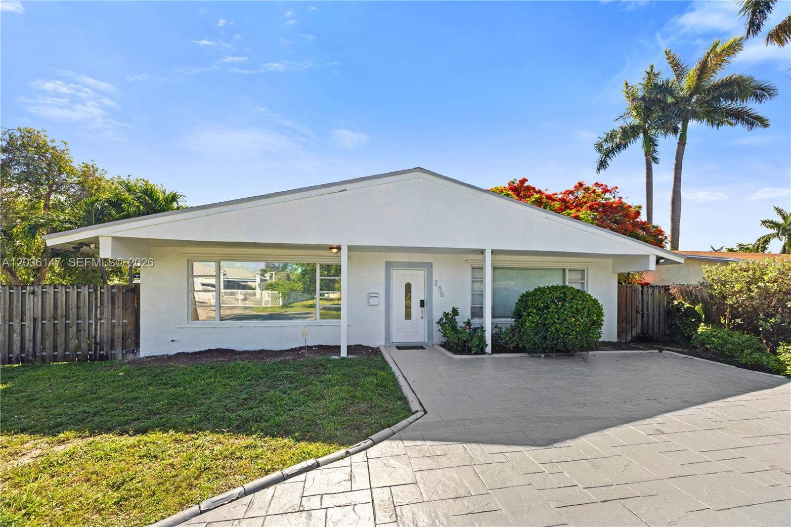 A white single-story house features a paved driveway, a front lawn, and palm trees — 230 NE 5th Ave, Dania Beach FL 33004, DANIA BEACH, FL