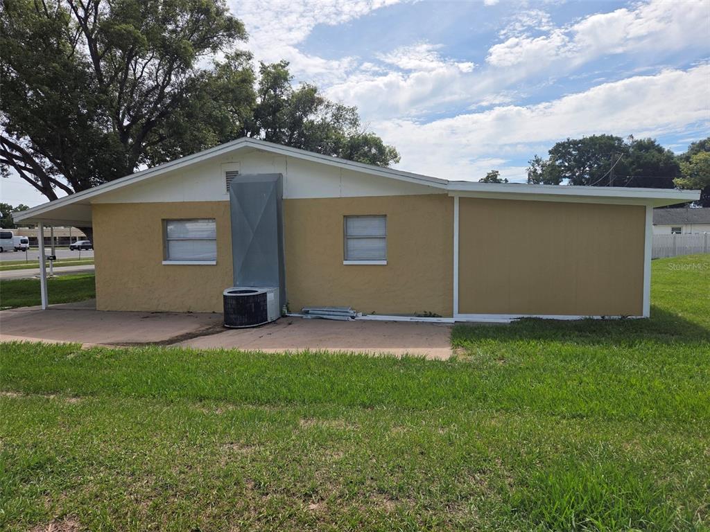 The exterior of a single-story house features a tan stucco wall, two windows, and an HVAC unit — 38300 HENRY DRIVE, ZEPHYRHILLS, FL