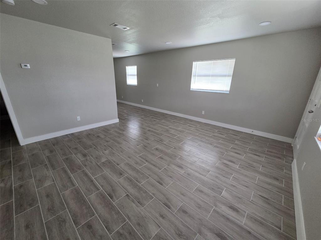 An empty room features gray wood-look tile flooring, light gray walls, and two windows — 38300 HENRY DRIVE, ZEPHYRHILLS, FL