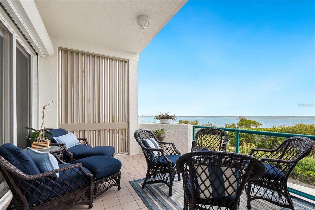 A covered balcony features wicker furniture and a view of the water — 340 GULF OF MEXICO DRIVE UNIT 115, LONGBOAT KEY, FL