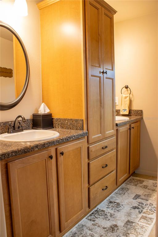A bathroom features a double vanity with light wood cabinets, dark countertops, and a tall tower — 5456 HOUSTON DRIVE, LAKELAND, FL