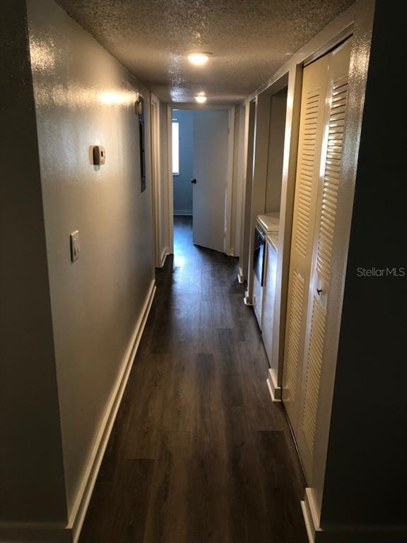 A hallway with wood-look flooring leads to a doorway, featuring a laundry closet on the right — 6519 W NEWBERRY ROAD UNIT 507, GAINESVILLE, FL