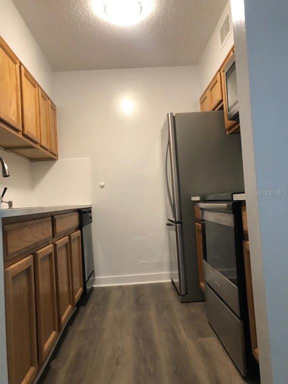 A galley kitchen features wood cabinets, stainless steel appliances, and wood-look flooring — 6519 W NEWBERRY ROAD UNIT 507, GAINESVILLE, FL