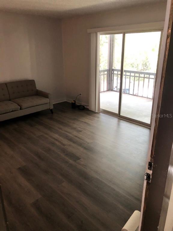 A living room features wood-look flooring, a gray sofa, and a sliding glass door to a balcony — 6519 W NEWBERRY ROAD UNIT 507, GAINESVILLE, FL