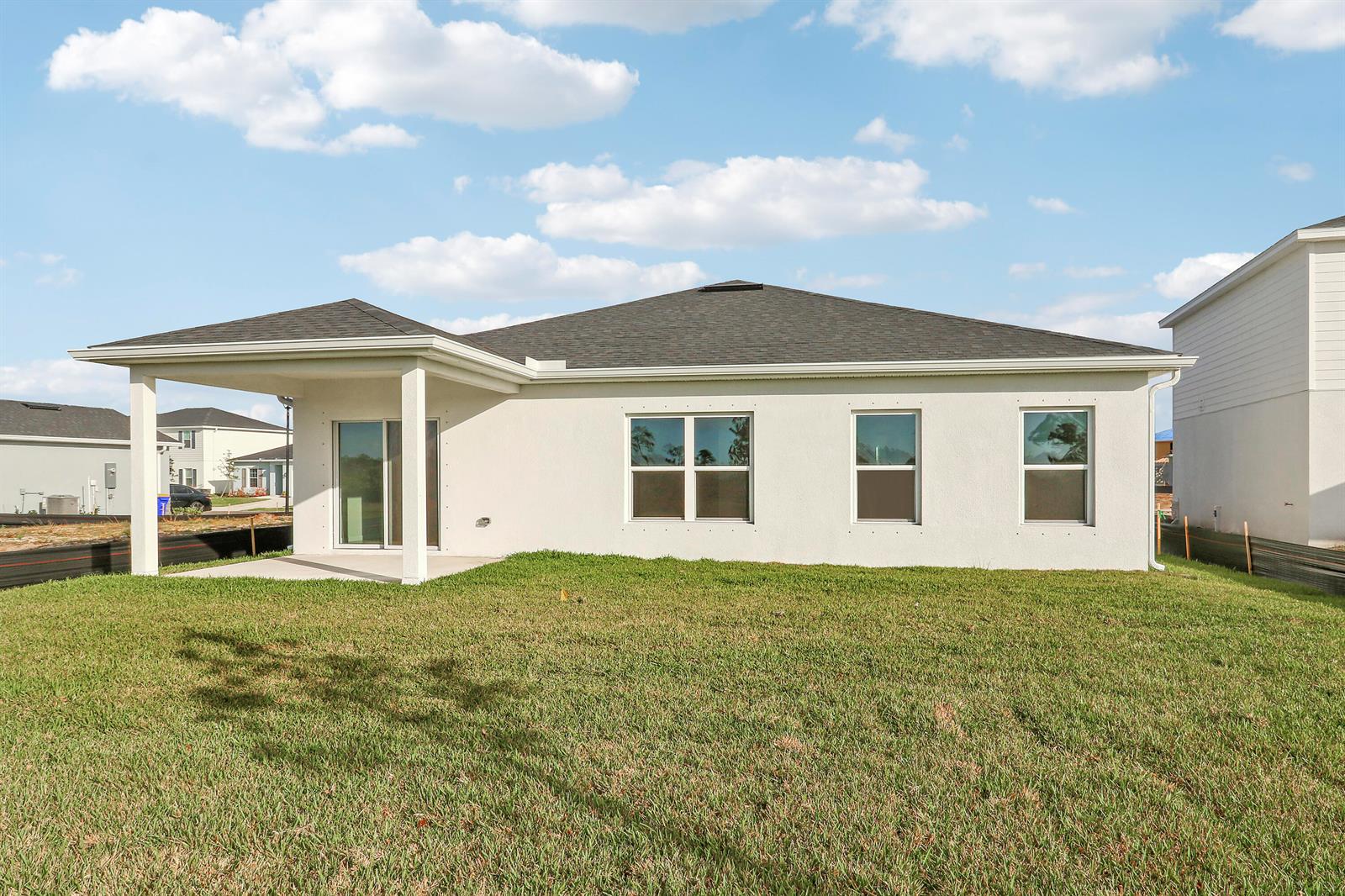 The rear exterior of a single-story house features a covered patio and a grassy yard — 15404 SW American Street, FL 34956, FL