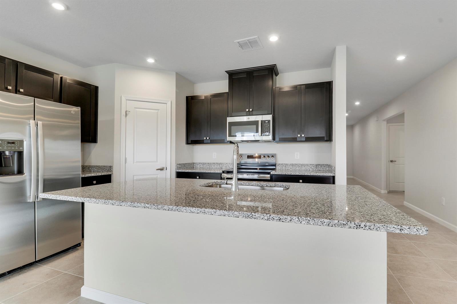 A kitchen features dark wood cabinets, granite countertops, a stainless steel refrigerator, and a central island — 15404 SW American Street, FL 34956, FL