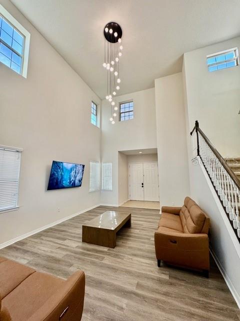 A high-ceilinged living room features a modern chandelier, wood-look flooring, and a staircase — 10264 HENBURY STREET, ORLANDO, FL