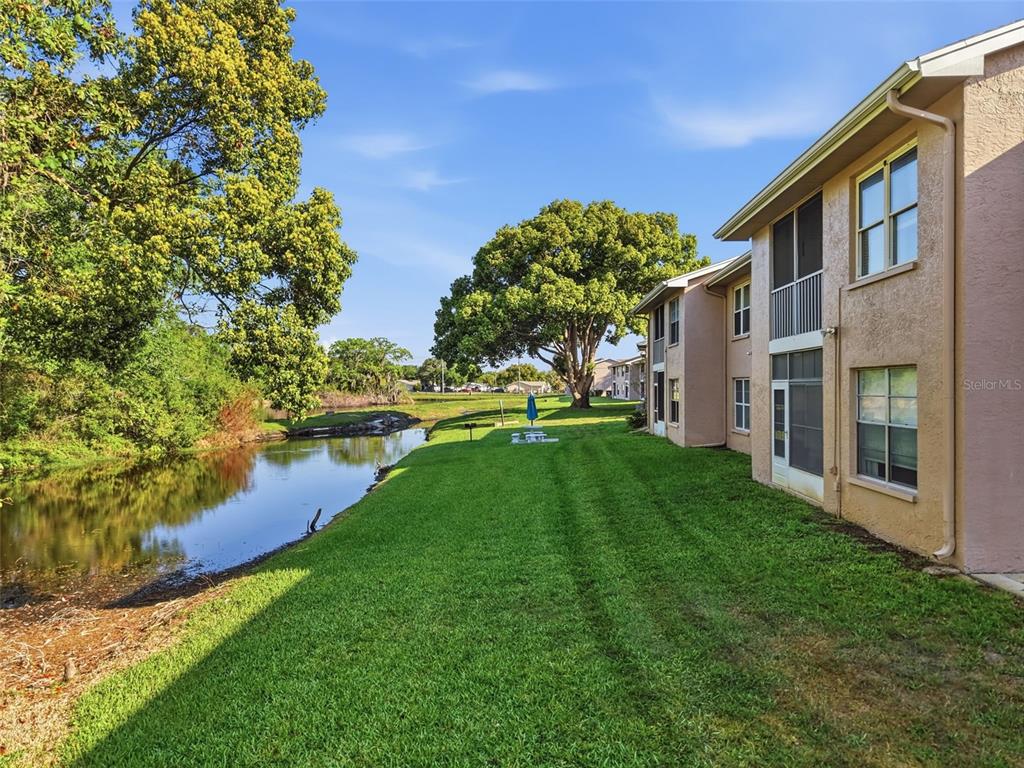 A multi-story apartment building sits beside a grassy lawn and a small pond — 4833 MYRTLE OAK DRIVE UNIT 12, NEW PORT RICHEY, FL