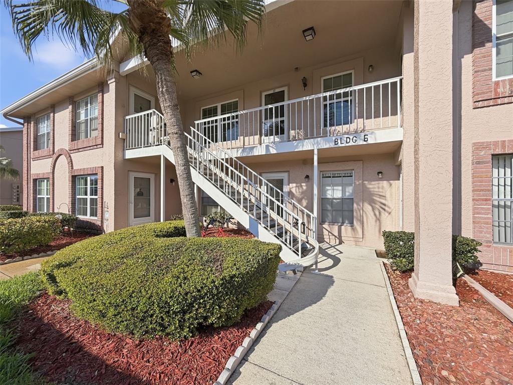 An exterior view of a two-story apartment building with a white metal staircase — 4833 MYRTLE OAK DRIVE UNIT 12, NEW PORT RICHEY, FL