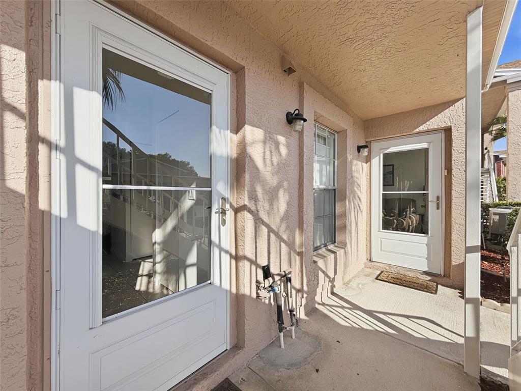 A stucco exterior features two white storm doors and a window on a concrete porch — 4833 MYRTLE OAK DRIVE UNIT 12, NEW PORT RICHEY, FL