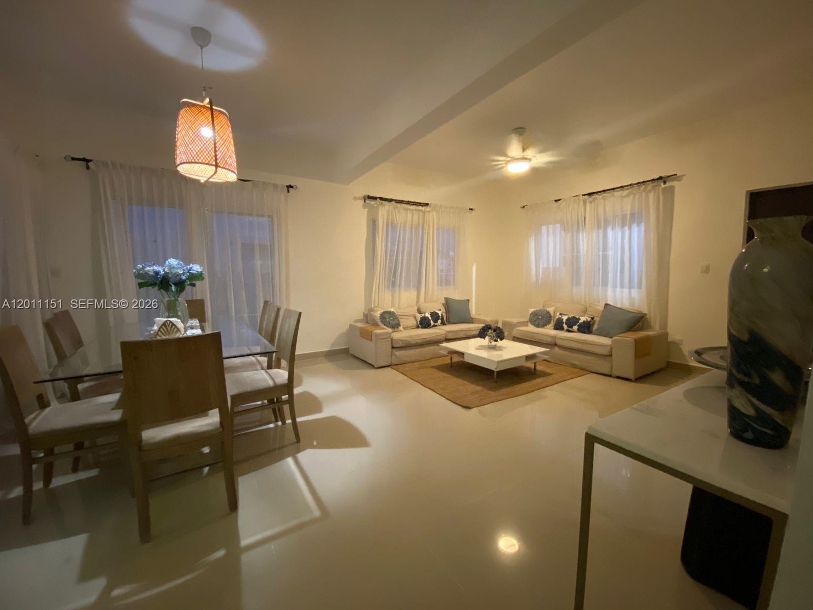 This open-concept living and dining area features tile floors, neutral furniture, and sheer curtains — M.71 Ciudad La Palma Dominican Republic, FL