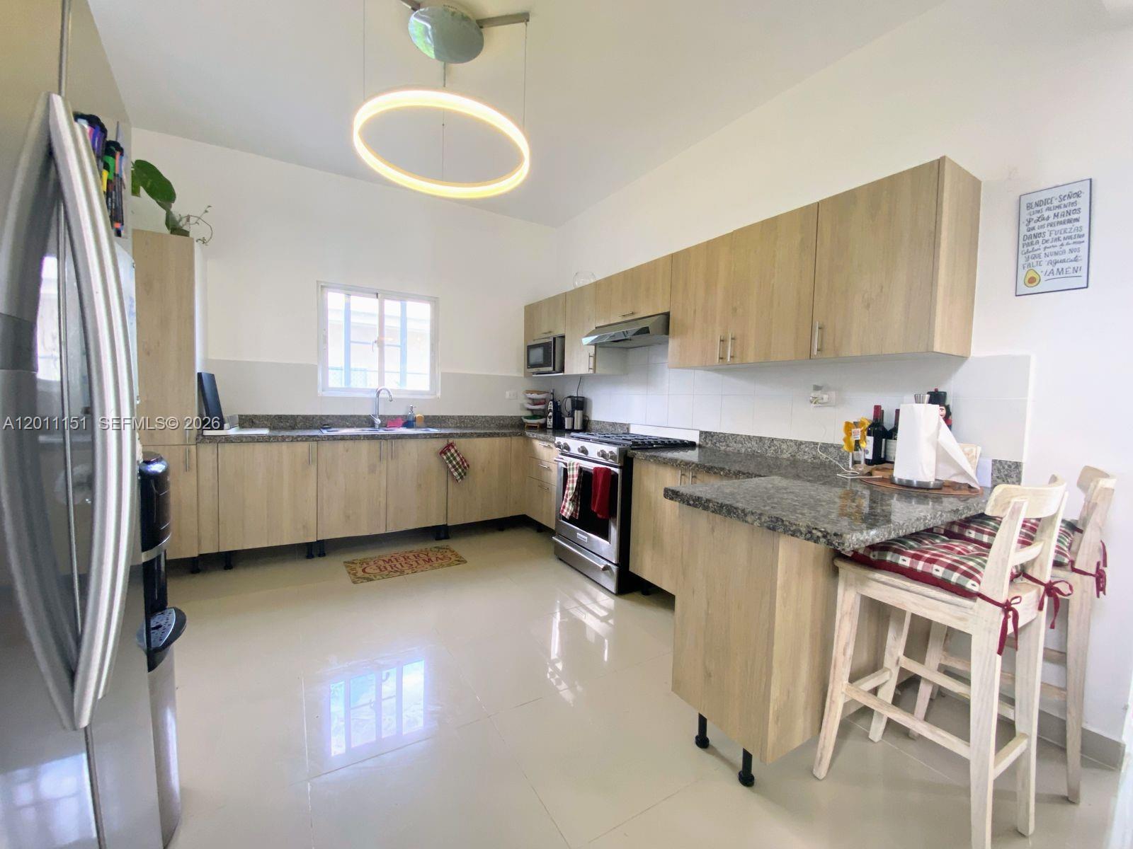 A kitchen features light wood cabinets, granite countertops, stainless steel appliances, and a breakfast bar — M.71 Ciudad La Palma Dominican Republic, FL