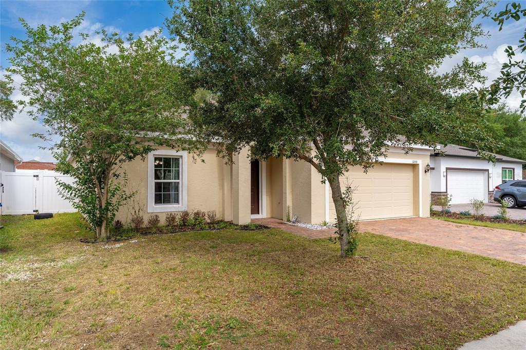 A single-story house with a tan stucco exterior, a two-car garage, and a front yard — 1209 STRATTON AVENUE, GROVELAND, FL
