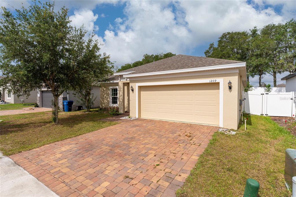 A single-story house with a beige stucco exterior, a two-car garage, and a brick driveway — 1209 STRATTON AVENUE, GROVELAND, FL