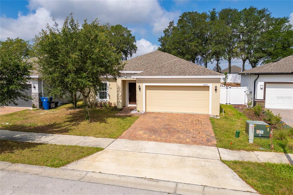 A single-story house with a tan stucco exterior, a brick paver driveway, and a garage — 1209 STRATTON AVENUE, GROVELAND, FL