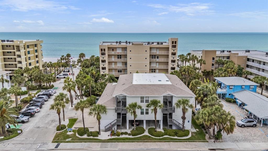 An aerial view shows a multi-story apartment building near the beach with parking lots — 1500 GULF BOULEVARD UNIT 204B, INDIAN ROCKS BEACH, FL