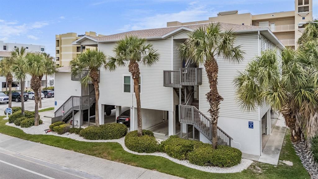 A two-story light-colored building with exterior staircases, palm trees, and ground-level parking — 1500 GULF BOULEVARD UNIT 204B, INDIAN ROCKS BEACH, FL