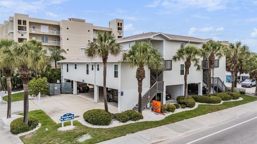 An elevated multi-unit residential building with palm trees and a parking area underneath — 1500 GULF BOULEVARD UNIT 204B, INDIAN ROCKS BEACH, FL