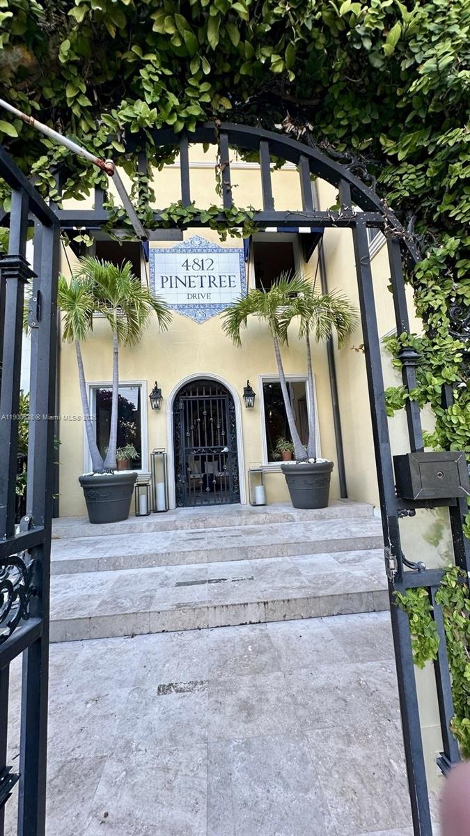 An arched metal gate opens to a stone staircase leading to a yellow building entrance — 4812 Pine Tree Dr # 204, Miami Beach FL 33140, MIAMI BEACH, FL