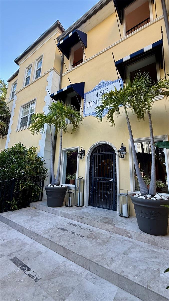 A yellow multi-story building exterior features a gated entrance, palm trees in pots, and awnings — 4812 Pine Tree Dr # 204, Miami Beach FL 33140, MIAMI BEACH, FL