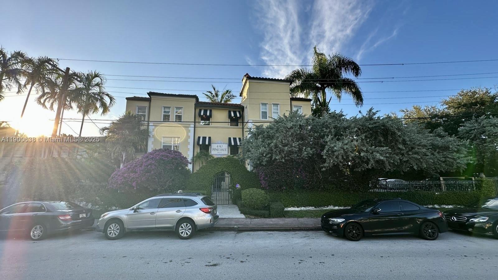 A three-story yellow building with black awnings stands behind a hedge and parked cars — 4812 Pine Tree Dr # 204, Miami Beach FL 33140, MIAMI BEACH, FL