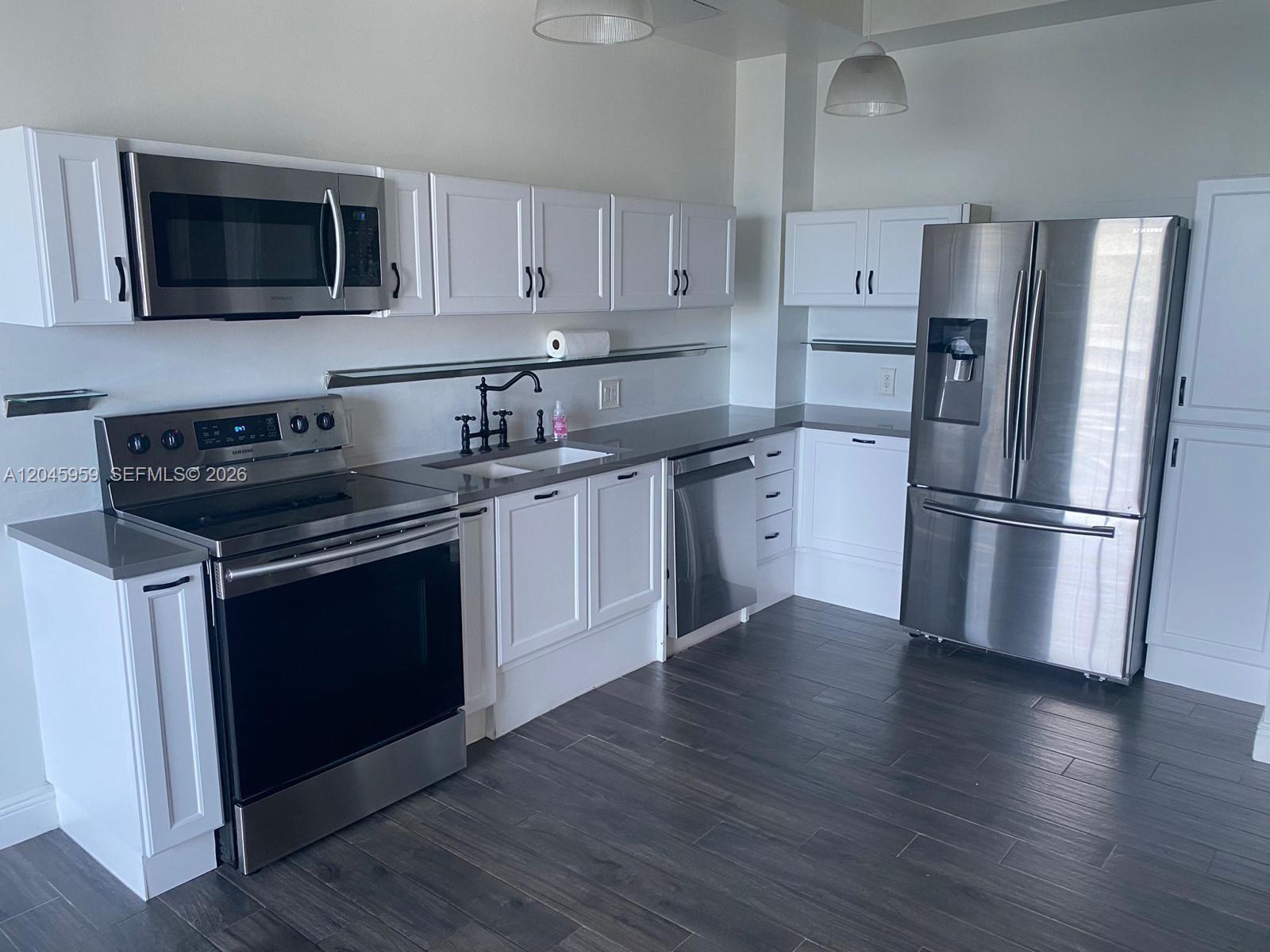A kitchen features white cabinetry, stainless steel appliances, gray countertops, and dark wood-look flooring — 10 SW South River Dr # 1708, Miami FL 33130, MIAMI, FL
