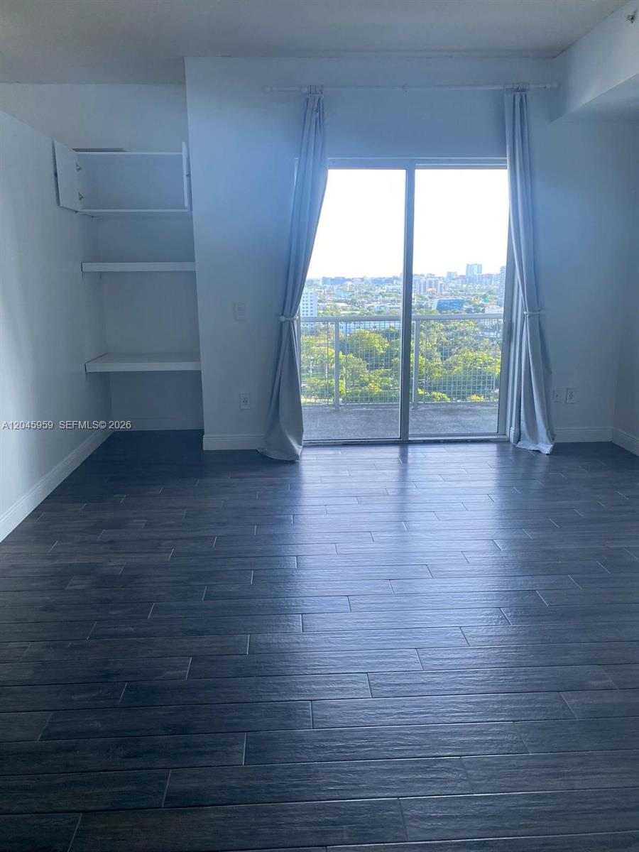 A room with dark wood-look flooring, built-in shelving, and a sliding glass door to a balcony — 10 SW South River Dr # 1708, Miami FL 33130, MIAMI, FL