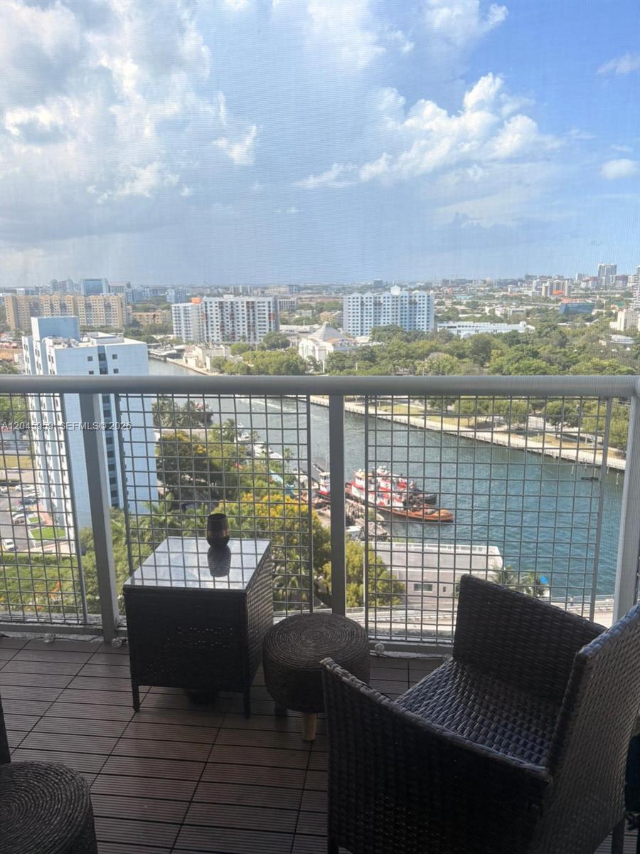 A balcony with wicker furniture overlooks a river, boats, and a city skyline — 10 SW South River Dr # 1708, Miami FL 33130, MIAMI, FL