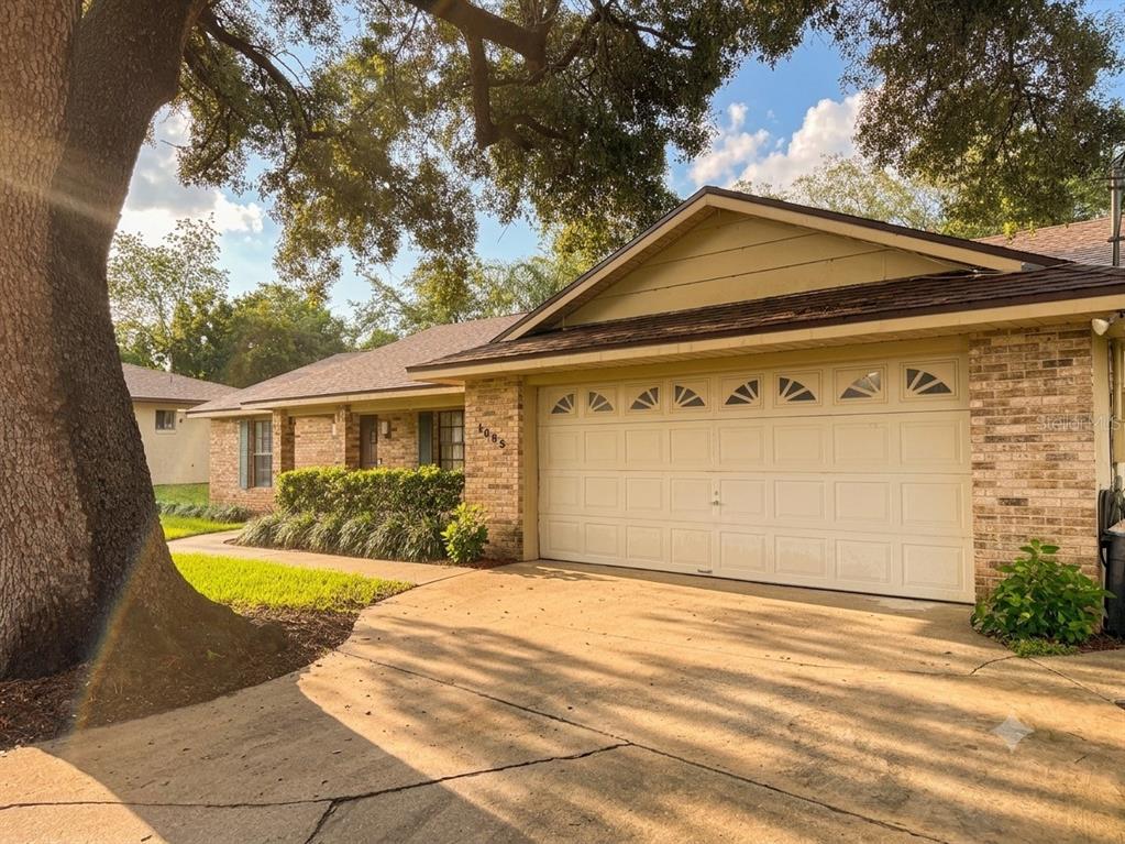 A single-story brick house with a two-car garage and a large tree in the yard — 1805 EXMORE AVENUE, DELTONA, FL