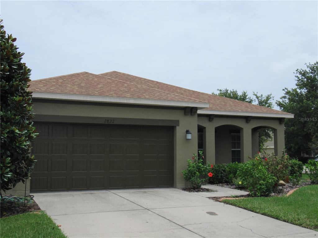 A single-story house with a brown stucco exterior, a two-car garage, and a covered entryway — 2822 MAPLE BROOK LOOP, LUTZ, FL