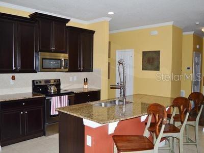 A kitchen features dark wood cabinets, granite countertops, a center island, and bar stool seating — 2822 MAPLE BROOK LOOP, LUTZ, FL