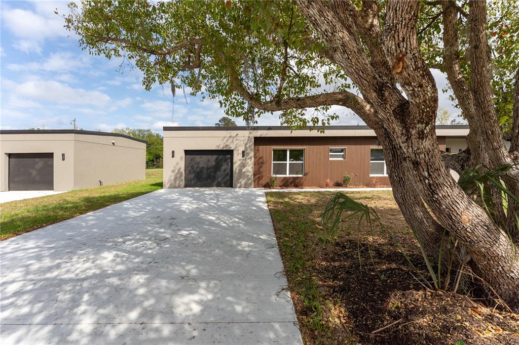 A modern single-story house with a concrete driveway and a large tree in the foreground — 457 RIVERVIEW AVENUE, SANFORD, FL