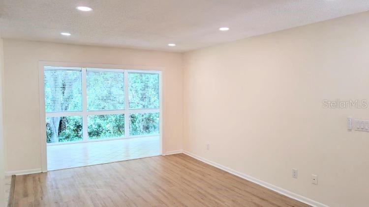 A bright living room features light wood-look flooring, recessed lighting, and a large window wall — 10 MASTERS COURT, PALM COAST, FL