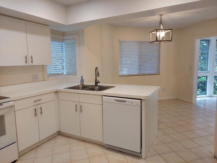 A kitchen with white cabinets, white appliances, and a tile floor, adjacent to a dining area — 10 MASTERS COURT, PALM COAST, FL