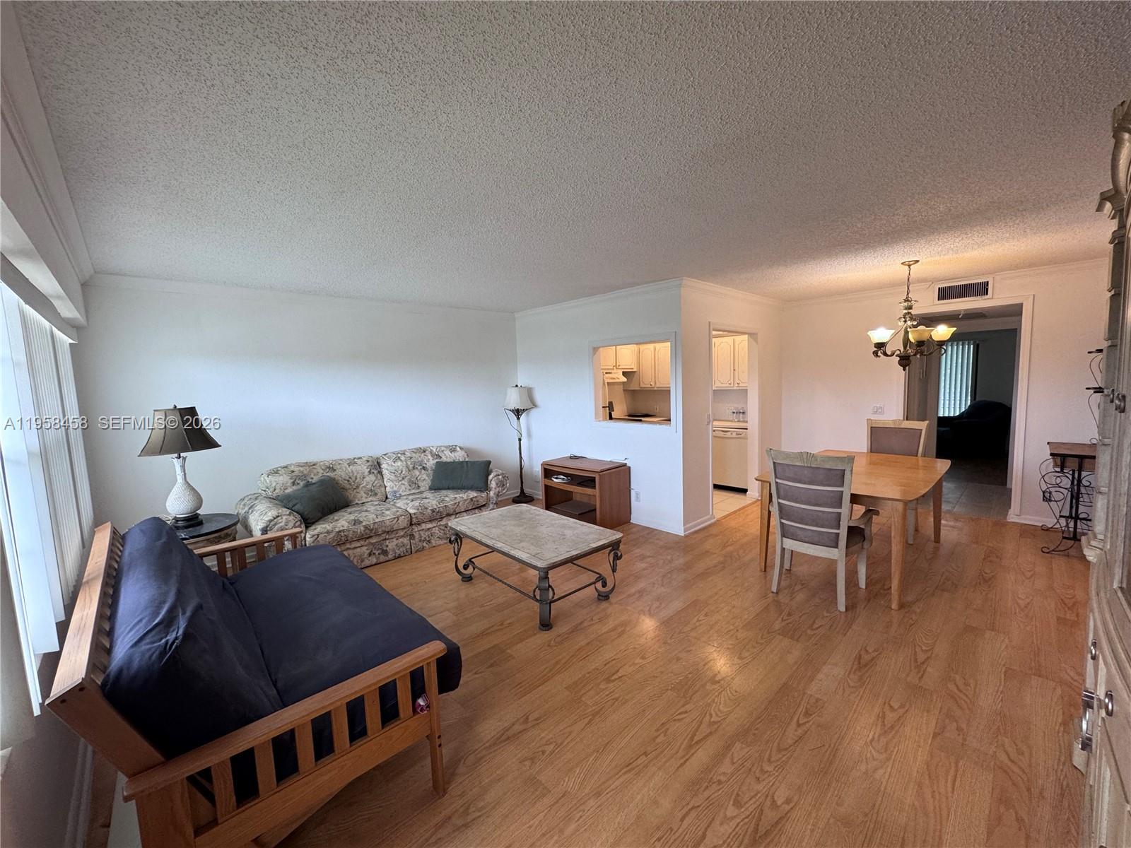 This open-concept living and dining area features wood-look flooring and a pass-through kitchen window — 293 Dorset # G, Boca Raton FL 33434, BOCA RATON, FL