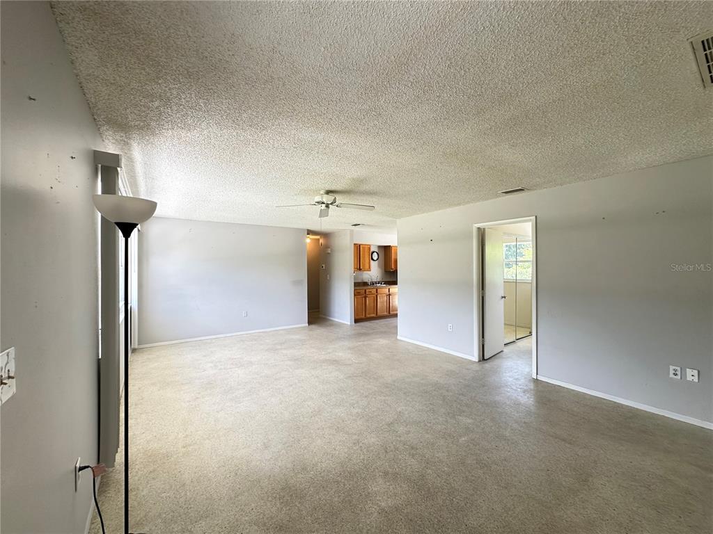 An open-concept living area features beige carpeting, a popcorn ceiling, and a view into the kitchen — 3543 DRANCE STREET, PUNTA GORDA, FL
