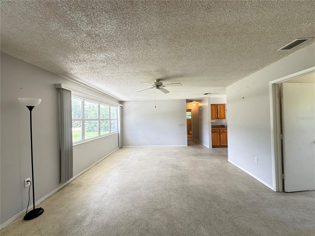 A living room with beige carpet, gray walls, a popcorn ceiling, and a ceiling fan — 3543 DRANCE STREET, PUNTA GORDA, FL