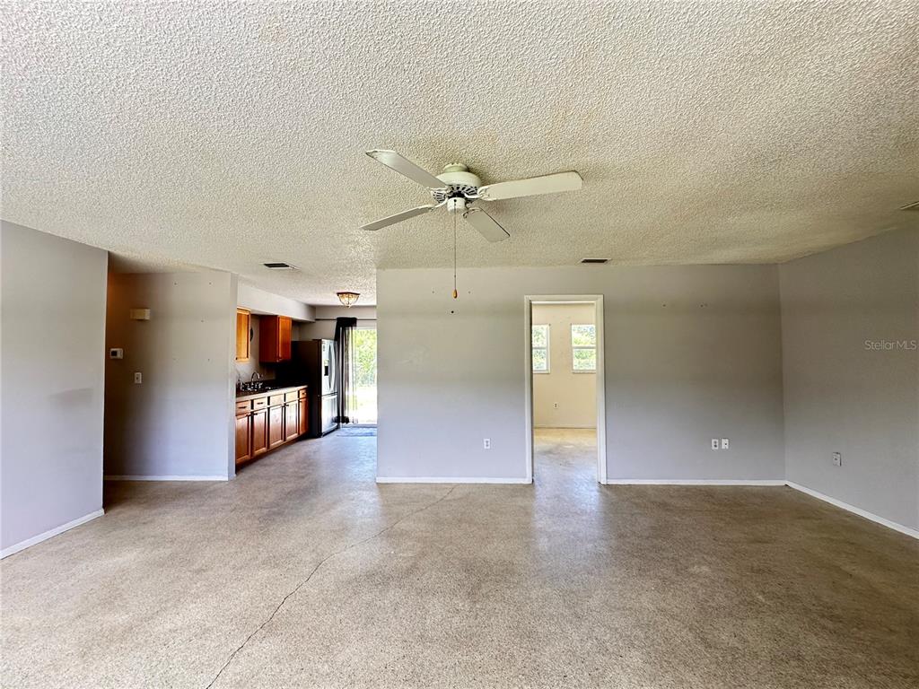 A spacious living area with a ceiling fan, concrete floors, and an adjacent kitchen — 3543 DRANCE STREET, PUNTA GORDA, FL
