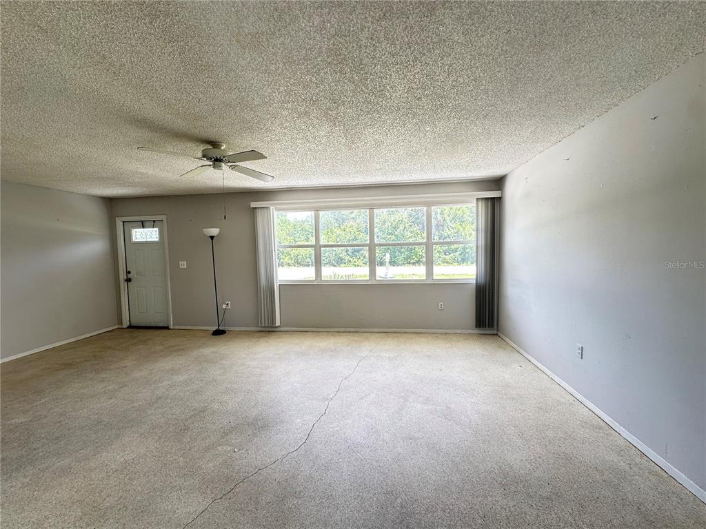 An empty living room features a popcorn ceiling, beige carpeting, and a large window — 3543 DRANCE STREET, PUNTA GORDA, FL
