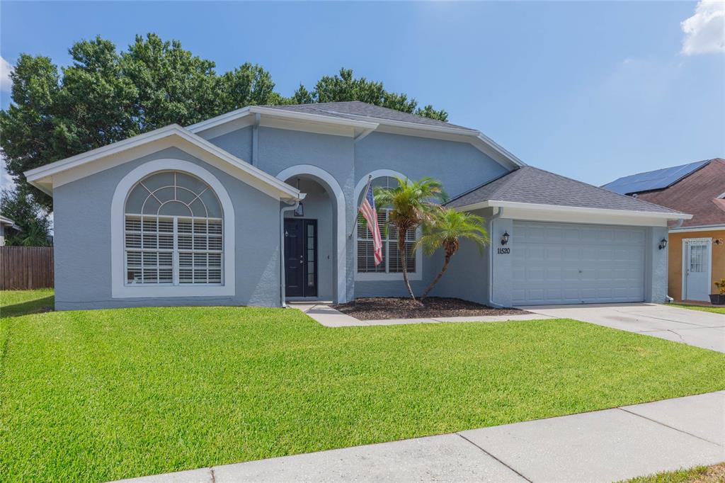 A single-story blue house with a two-car garage, arched windows, and a front lawn — 11520 WELLMAN DRIVE, RIVERVIEW, FL