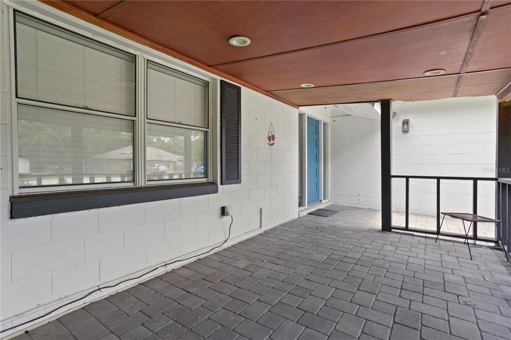 A covered patio features gray paver flooring, a wood-paneled ceiling, and a blue front door — 2412 GRANDVIEW AVENUE, SANFORD, FL