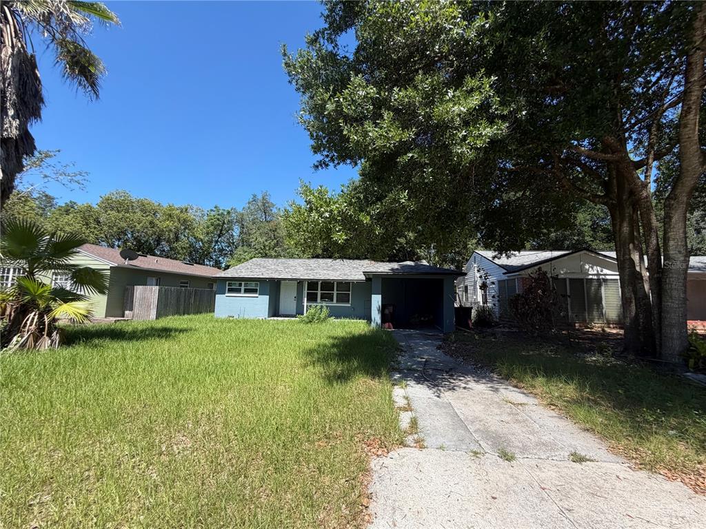 A single-story gray house with a carport and an overgrown lawn under large trees — 116 S GLENWOOD AVENUE, ORLANDO, FL