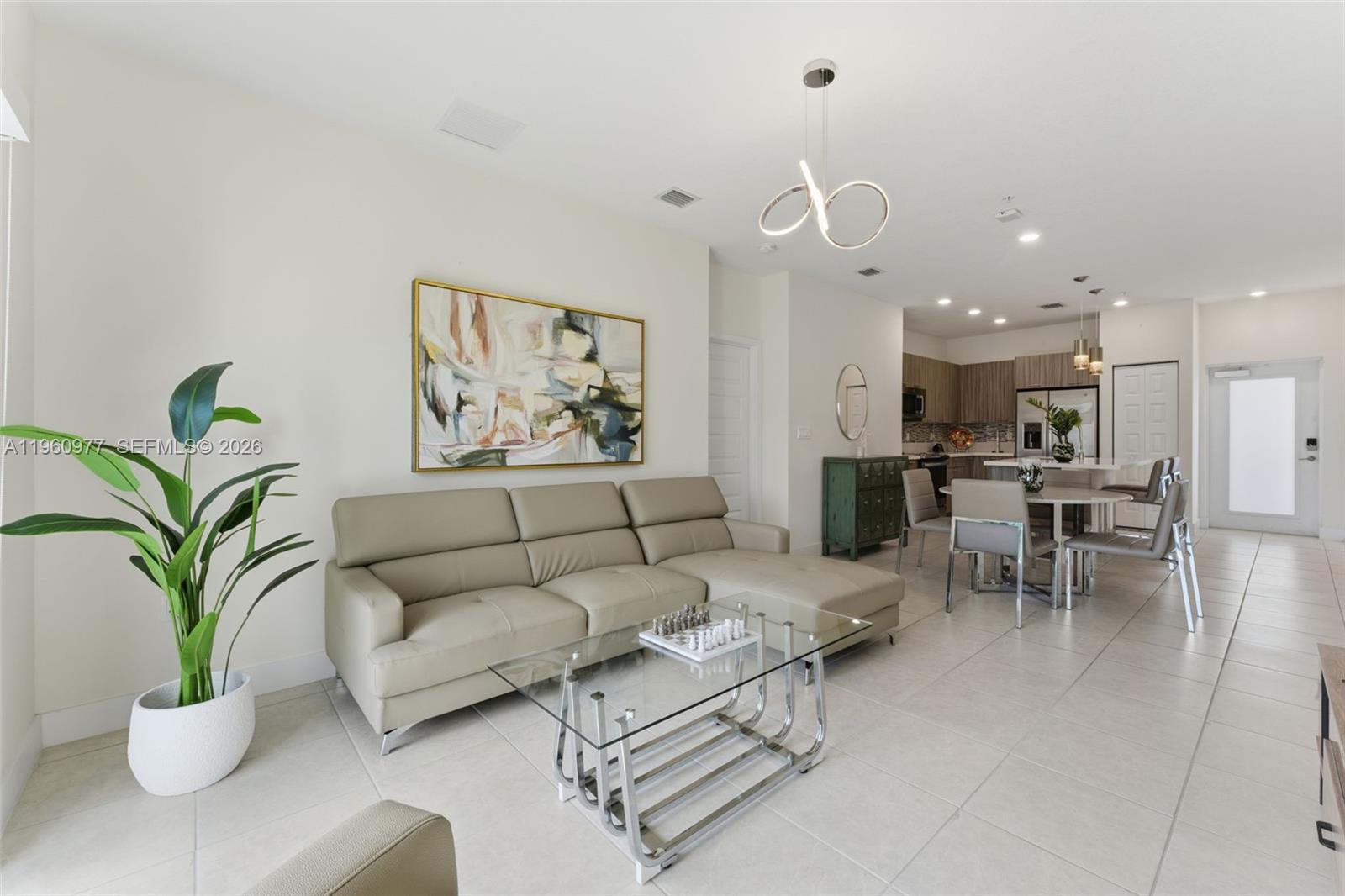 A modern open-concept living and dining area features a beige sectional, glass table, and kitchen — 8301 NW 41st St # 407, Doral FL 33166, DORAL, FL
