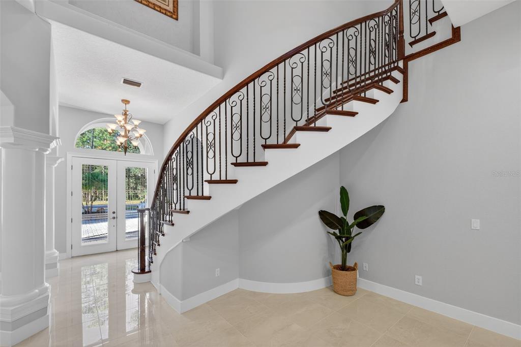 A curved staircase with a dark wood railing and iron balusters sits in a tiled foyer — 13950 SMOKERISE COURT, ORLANDO, FL