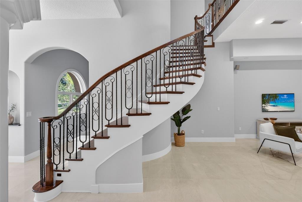 A curved staircase with dark wood handrails and decorative metal balusters sits in a foyer — 13950 SMOKERISE COURT, ORLANDO, FL